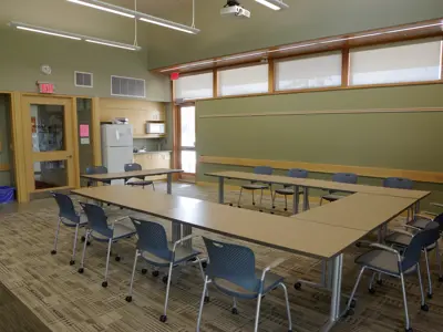 A community room with tables configured in a horseshoe shape with chairs around them